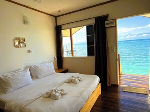 Una habitación de hotel con una cama, un ventanal con vista al mar y piso de madera.