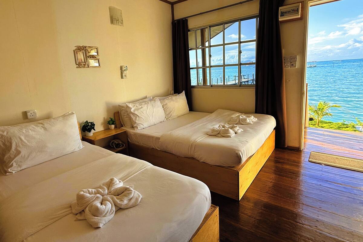 Habitación de hotel con dos camas, un ventanal con vistas al mar y suelo de madera.