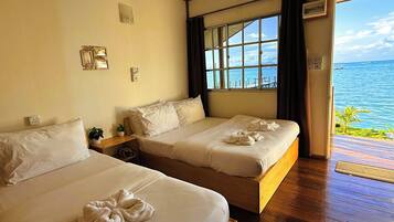 A hotel room with two beds, a large window with a view of the sea, and a wooden floor.