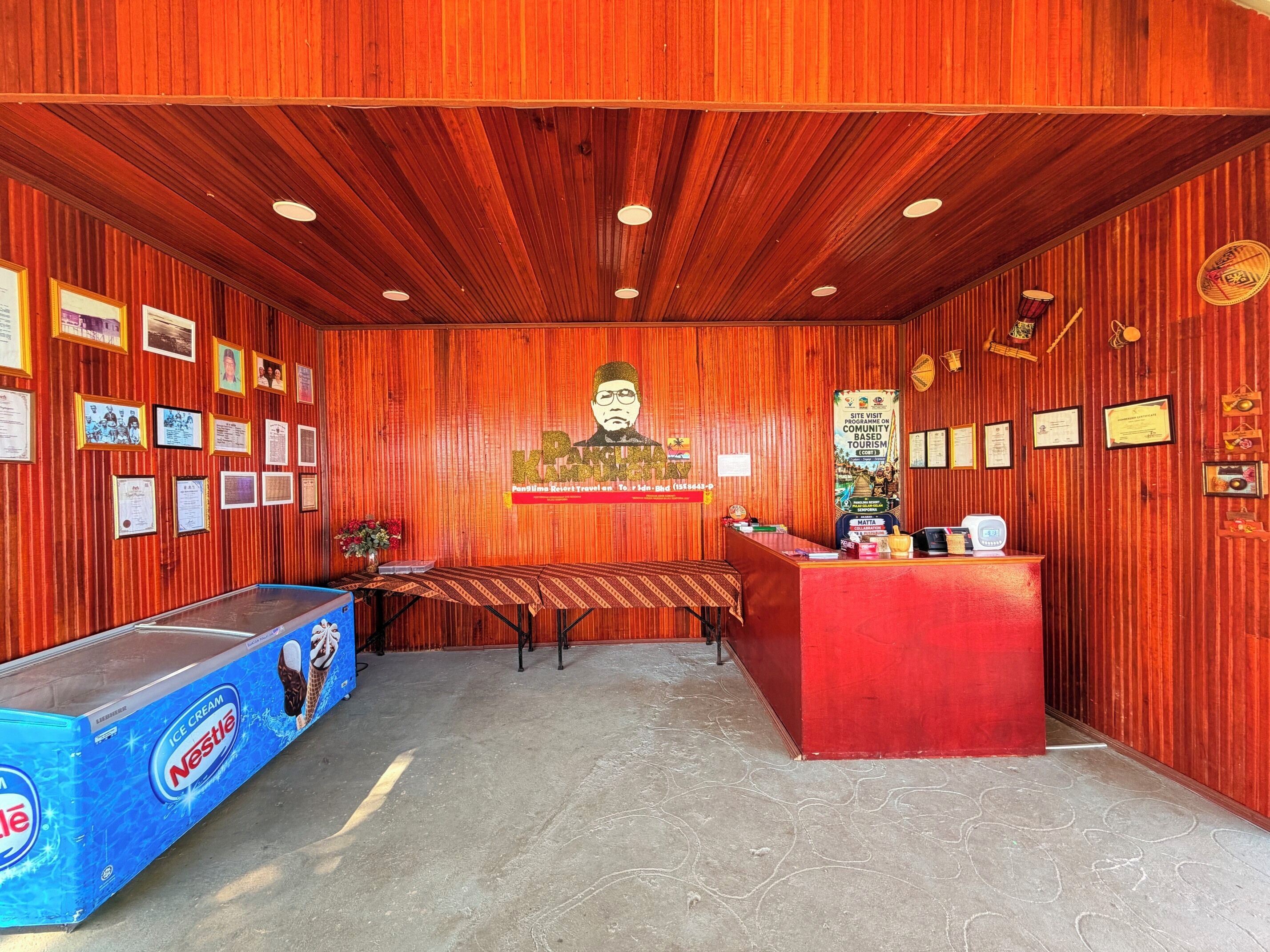 Un área de recepción con techo de madera, un banco, un mostrador y una pared decorada con certificados y documentos enmarcados.