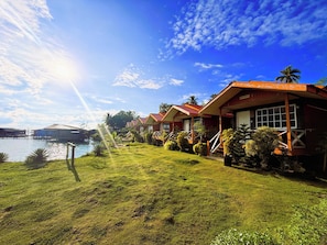 A row of wooden cabins with a grassy lawn and a body of water in the background. - Panglima Resort Bum Bum Island, Semporna (Bum Bum Island)