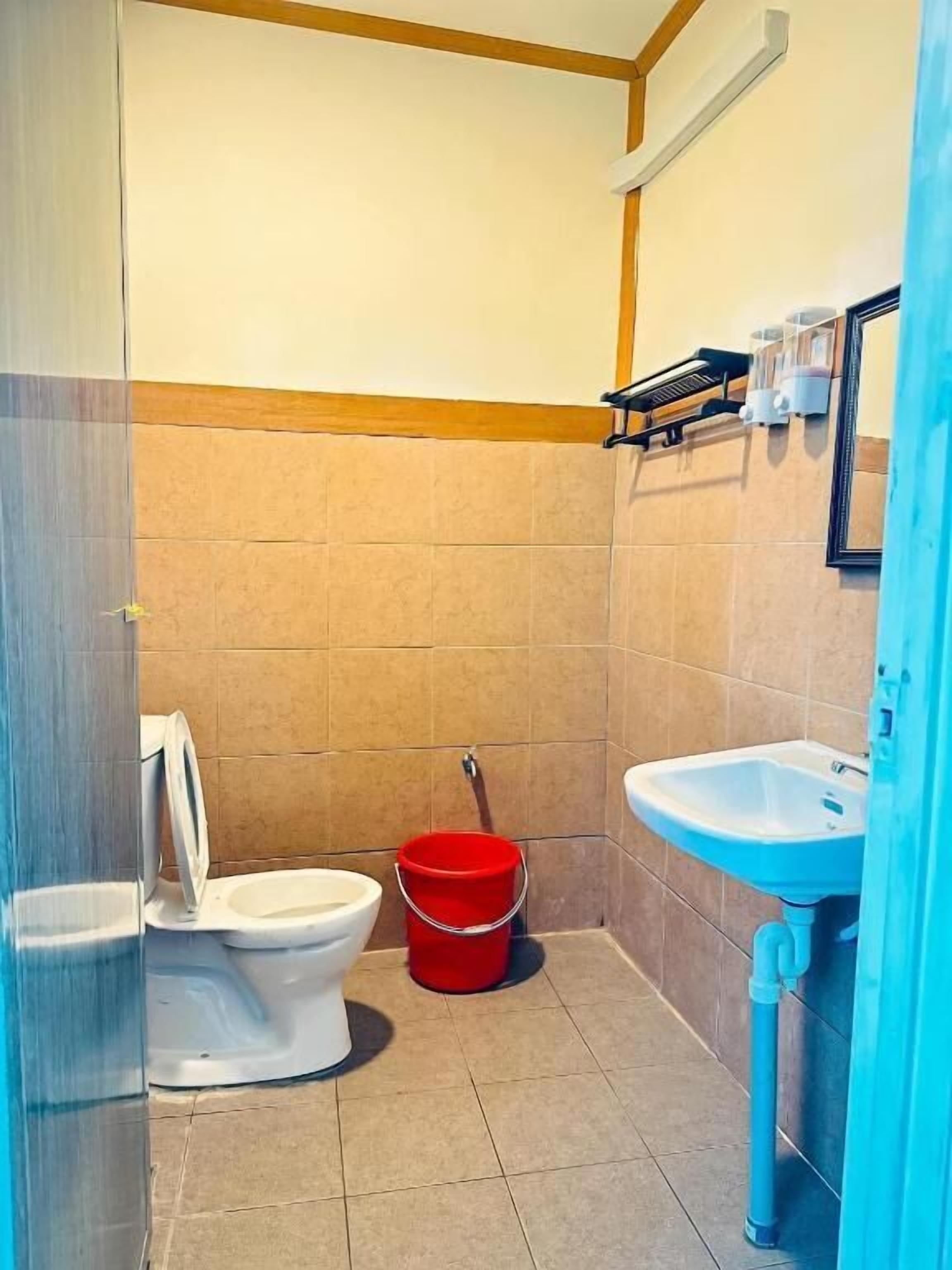 A small bathroom with a toilet, a red bucket, and a sink.