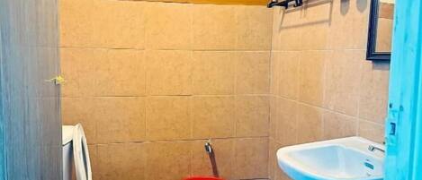 A small bathroom with a toilet, a red bucket, and a sink.