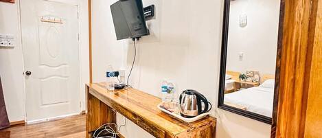 A hotel room with a wooden floor, a wooden bench, a TV mounted on the wall, a mirror, and a door with a handle.