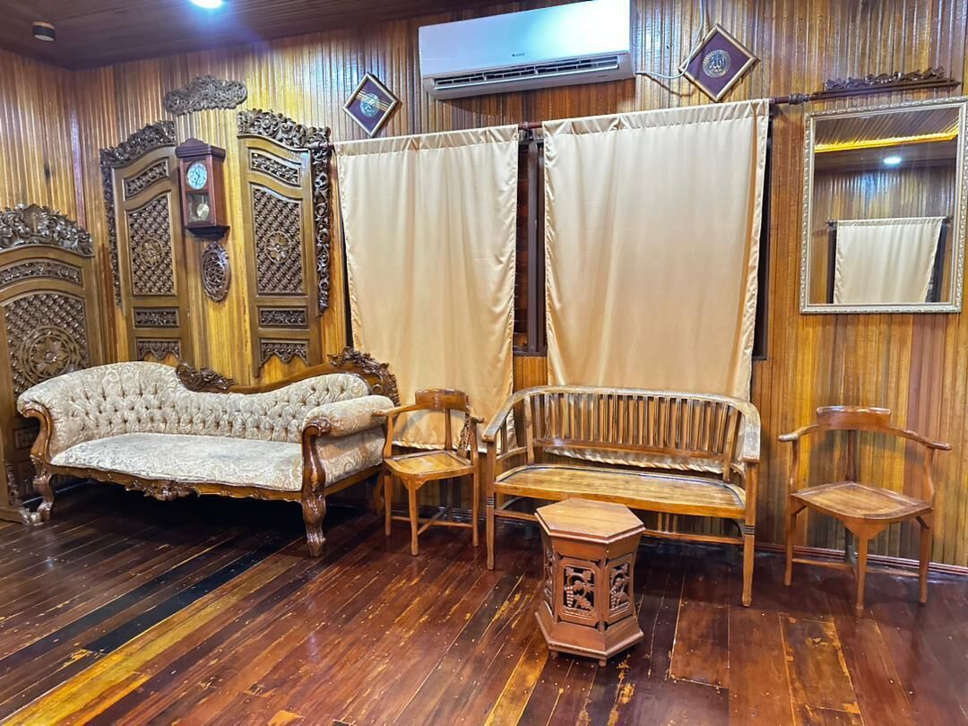 Una habitación con piso de madera, un sofá capitonado, un banco de madera y una pequeña mesa.