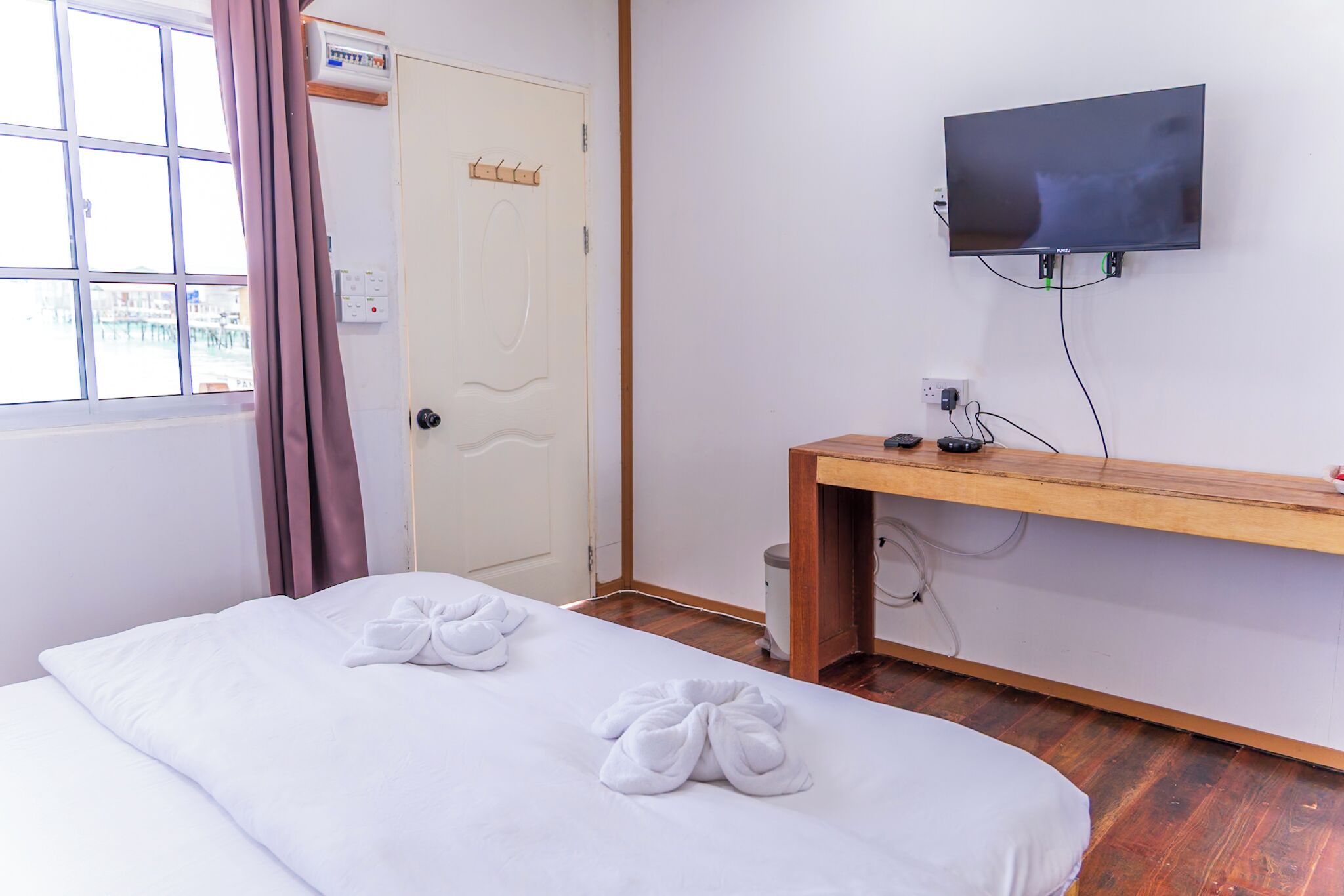 A hotel room with a bed, a TV mounted on the wall, and a wooden desk.