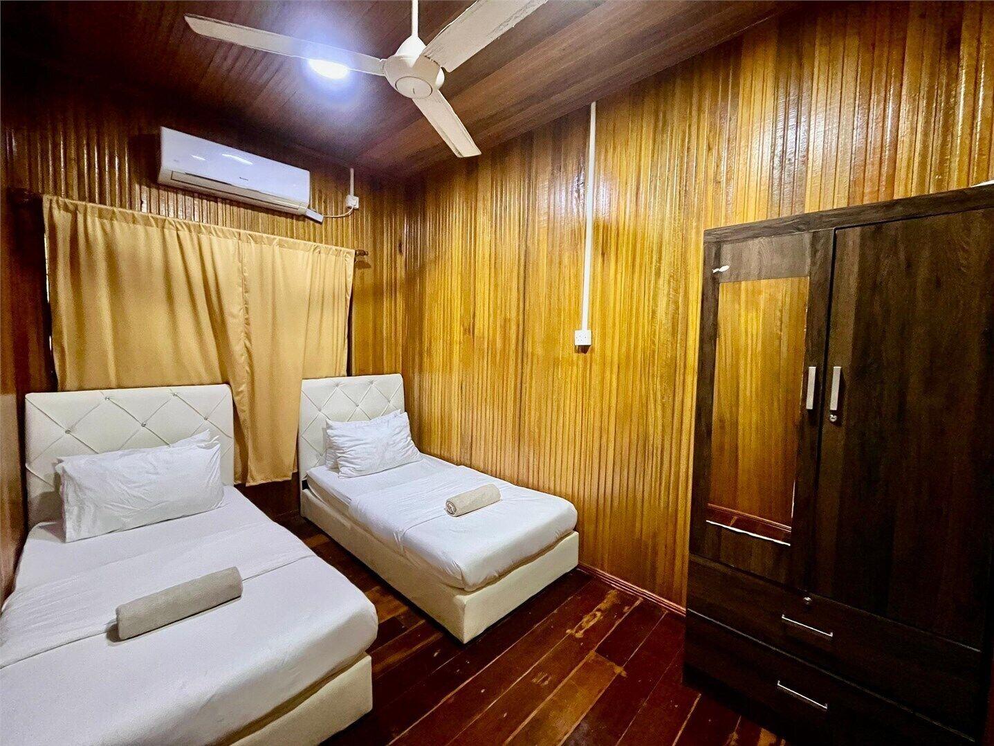 A room with two single beds, a wardrobe, a ceiling fan, and an air conditioning unit.