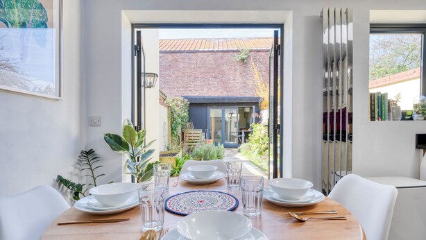 A dining area with a table set for four, a view of a brick building, and a bookshelf with books and decorative items.