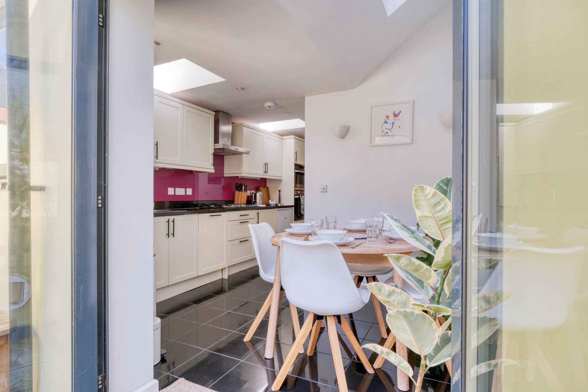 A modern kitchen with white cabinets, a pink accent wall, and a dining area with a round table and white chairs.