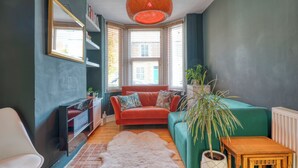 A cozy living room with a red sofa, a white chair, a large plant, and a wooden table.