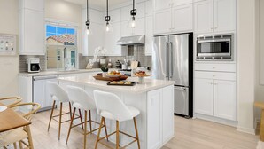 A modern kitchen with white cabinetry, stainless steel appliances, and a central island with bar stools. - Modern Grand Luxury Estate in Irvine with Pool & Amenities  (Irvine)