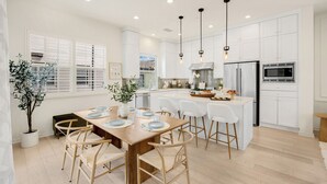 A modern kitchen with white cabinetry, a wooden dining table, and bar stools. - Modern Grand Luxury Estate in Irvine with Pool & Amenities  (Irvine)