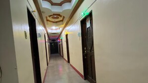Un couloir d’hôtel avec un sol carrelé, des encadrements de porte en bois et un plafond décoratif.