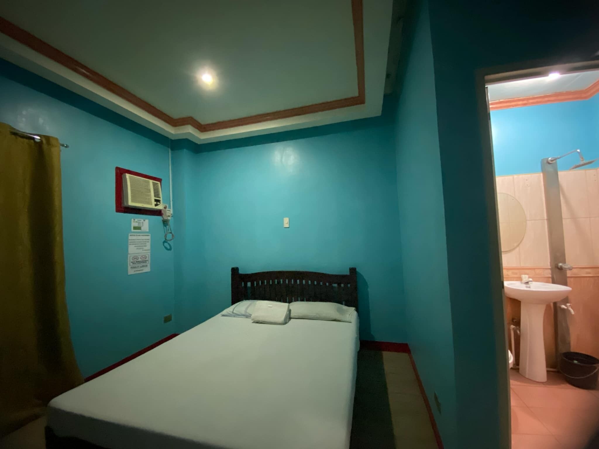 Ein Zimmer mit einem Einzelbett, einer Wand-Klimaanlage und einem sichtbaren Badezimmer mit Waschbecken und Toilette.