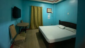 Une pièce comprenant un lit, un téléviseur fixé au mur, une table avec une chaise et un rideau.