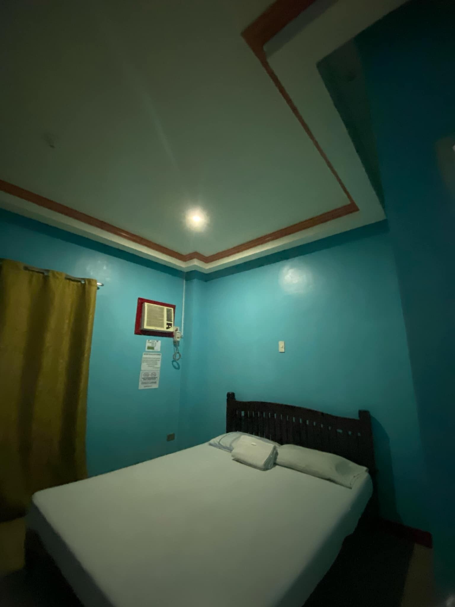 A room with a bed, a wall-mounted air conditioning unit, and a curtain.