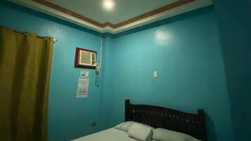 A room with a bed, a wall-mounted air conditioning unit, and a curtain.