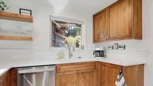 A modern kitchen with wooden cabinets, a white countertop, a built-in dishwasher, and a window providing a view of the outside. - Charming Historical Home in Downtown Boise (Boise)