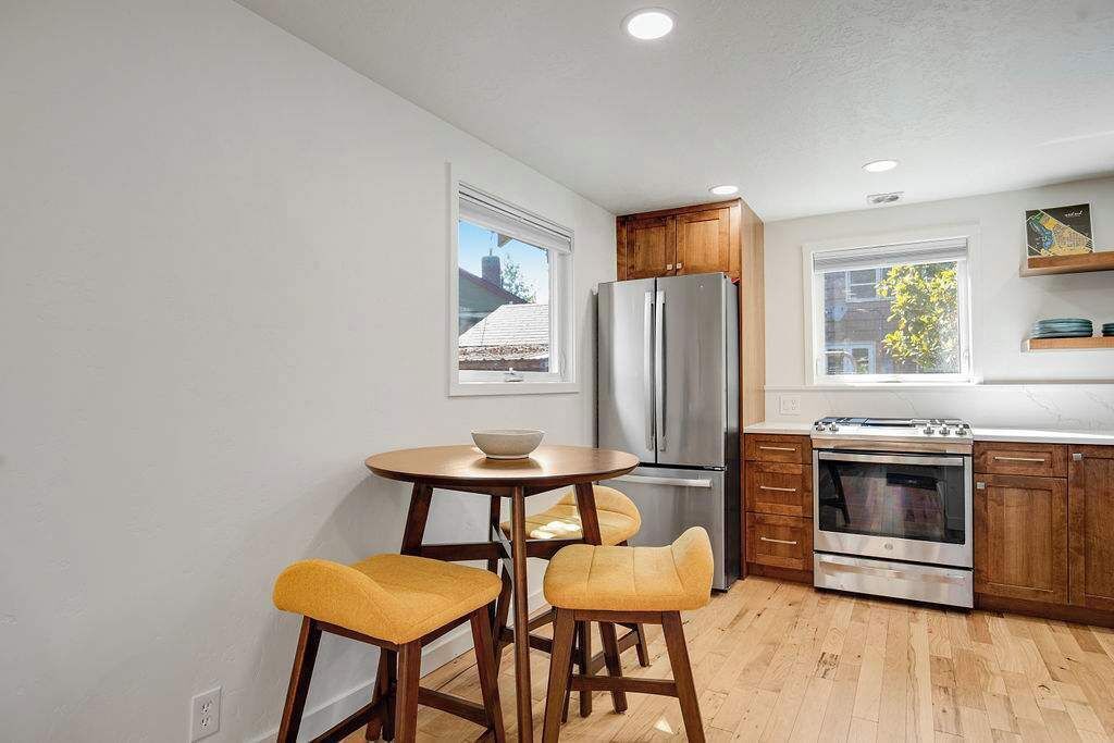 A modern kitchen with wooden cabinets, a stainless steel refrigerator, an oven, and a round dining table with two chairs.