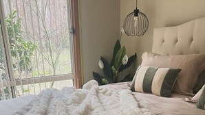 Une chambre avec un grand lit, un luminaire suspendu et une vue sur la verdure.