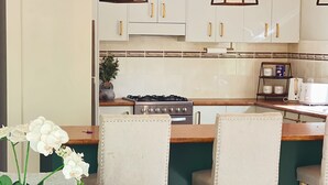 Une cuisine moderne avec des meubles blancs, une cuisinière à gaz et deux luminaires suspendus.