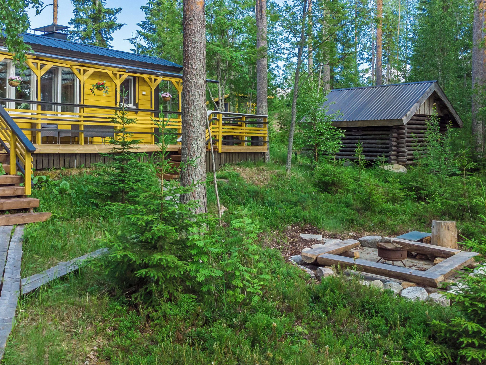 A yellow cabin with a deck and a log cabin in a forested area.