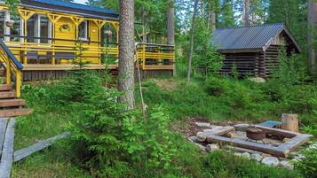 A yellow cabin with a deck and a log cabin in a forested area.