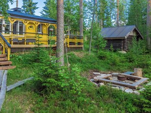 A yellow cabin with a deck and a log cabin in a forested area.