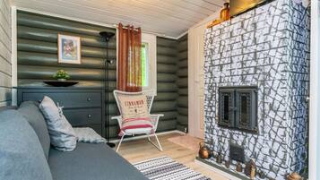 A cozy log cabin interior with a fireplace, a sofa, a chair, and a small table with a plant.