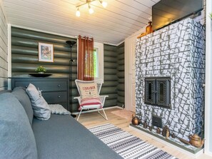A cozy log cabin interior with a fireplace, a sofa, a chair, and a small table with a plant.
