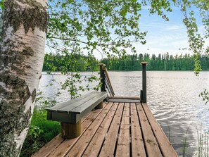 Une jetée en bois avec un banc, une rambarde et une vue sur un lac entouré d’arbres.