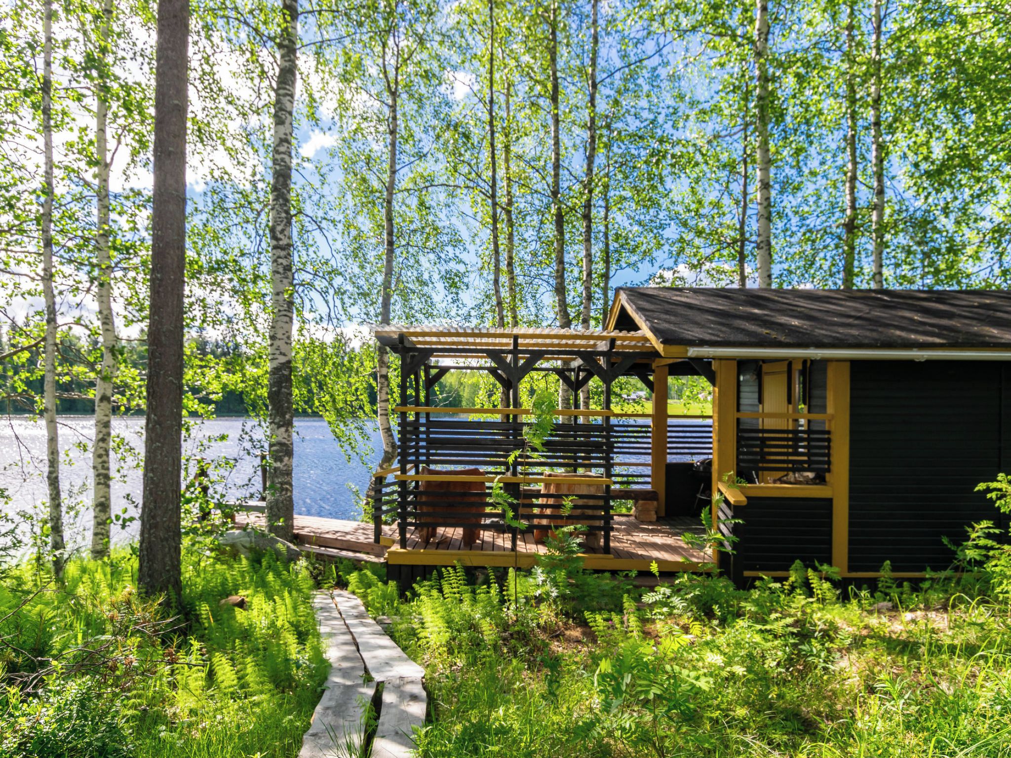 A cabin with a wooden deck overlooking a lake, surrounded by trees.