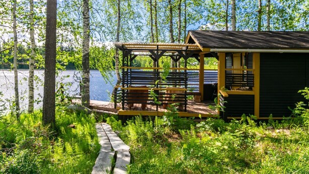 A cabin with a wooden deck and a covered seating area overlooking a lake. - Lammenranta by Interhome (Rautalampi)