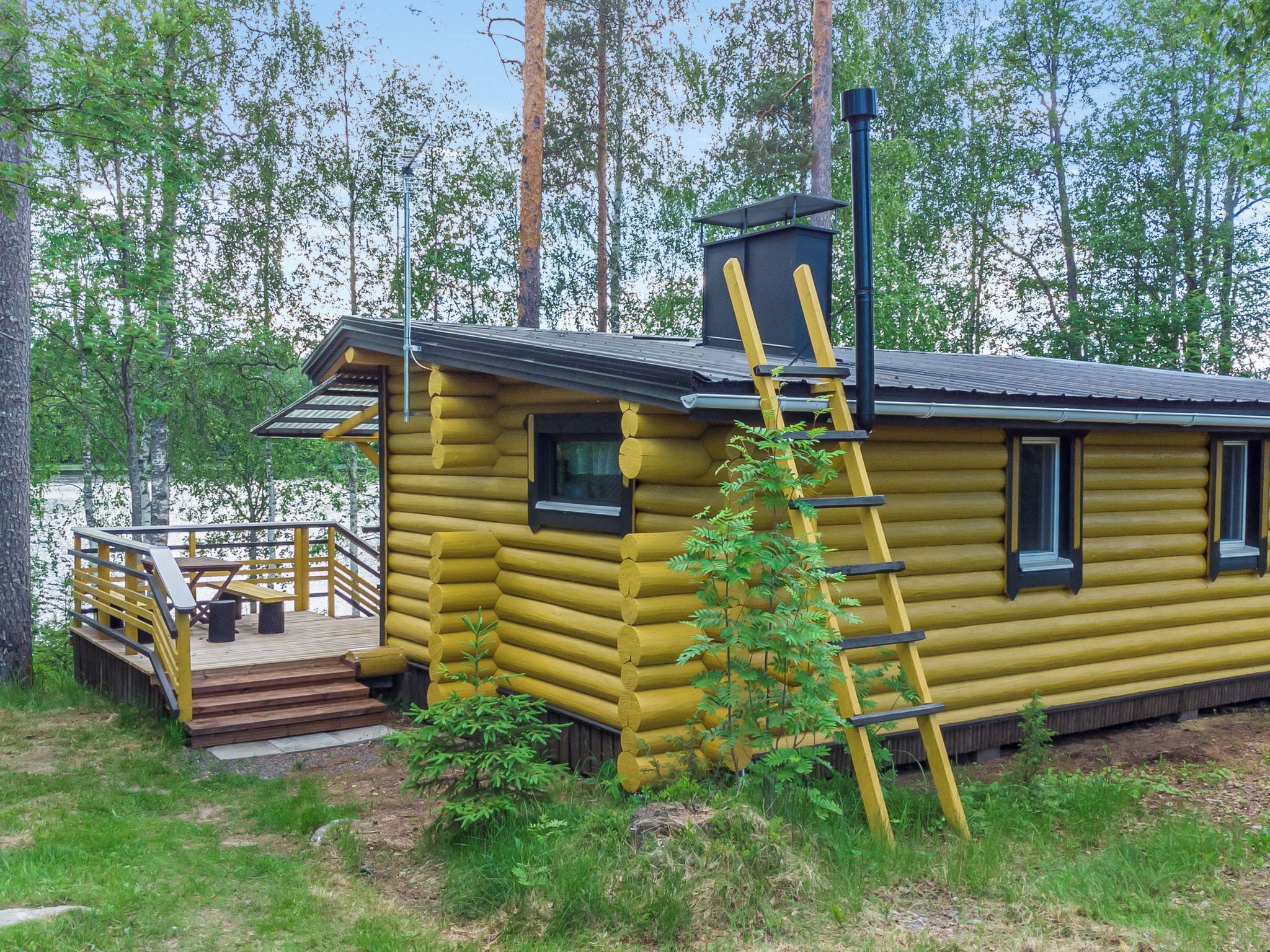 A log cabin with a wooden deck, a set of stairs, and a ladder.