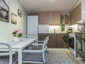 Une cuisine compacte avec un réfrigérateur blanc, un four à micro-ondes et une cuisinière. On y trouve une table à manger avec des chaises et un vase de fleurs.