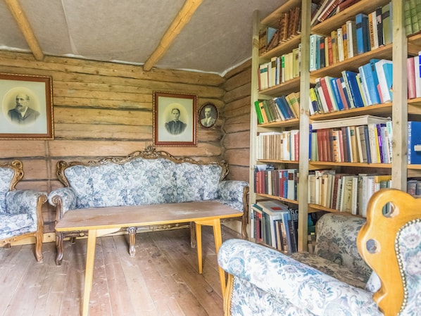 A room with a wooden ceiling, a sofa, a table, and a bookshelf filled with books.