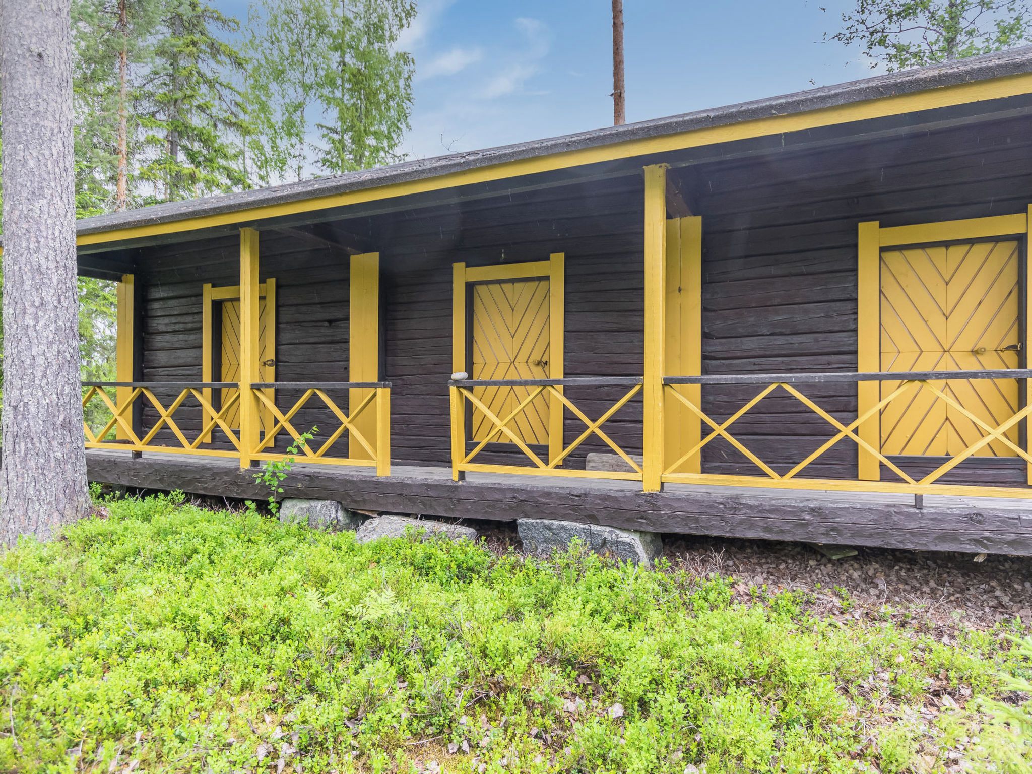 Un bâtiment en bois avec des portes et des balustrades jaunes, entouré de verdure.
