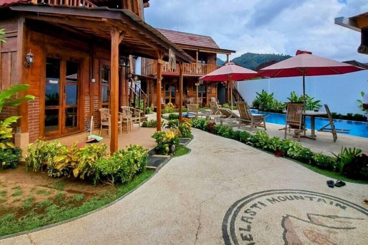A wooden building with a red roof, a pool area with lounge chairs and umbrellas, and a pathway leading to the entrance.