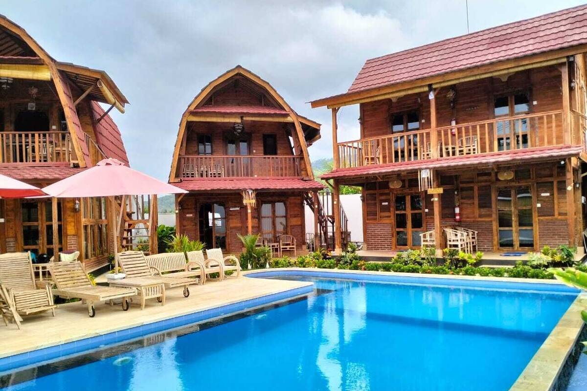 A pool area with wooden buildings, lounge chairs, and umbrellas.