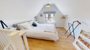 Een slaapkamer met een bed, nachtkastje, lamp, raam en een plank met zeeschelpen.