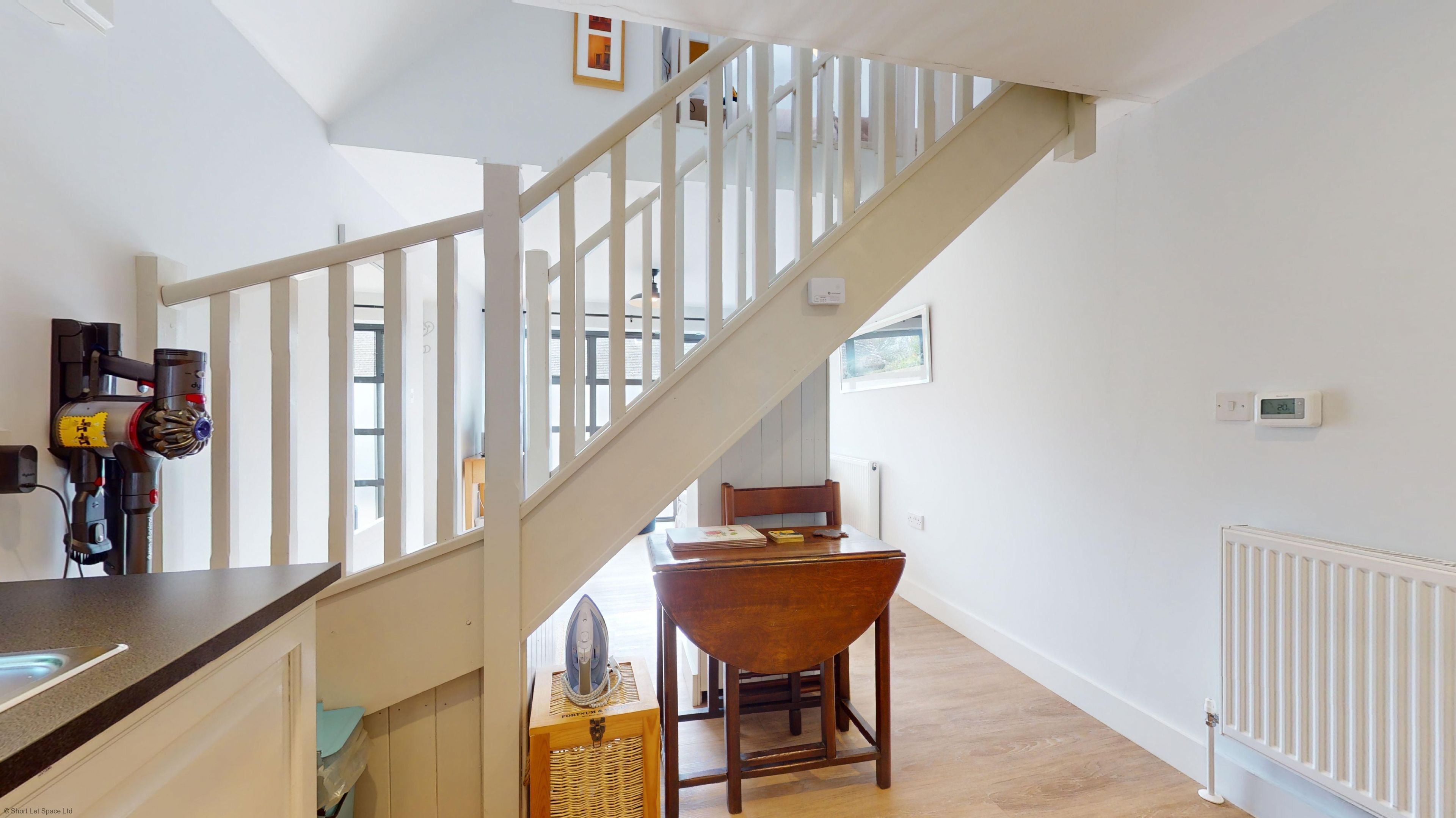 A staircase with white railings leading to a room with a wooden table and chairs.