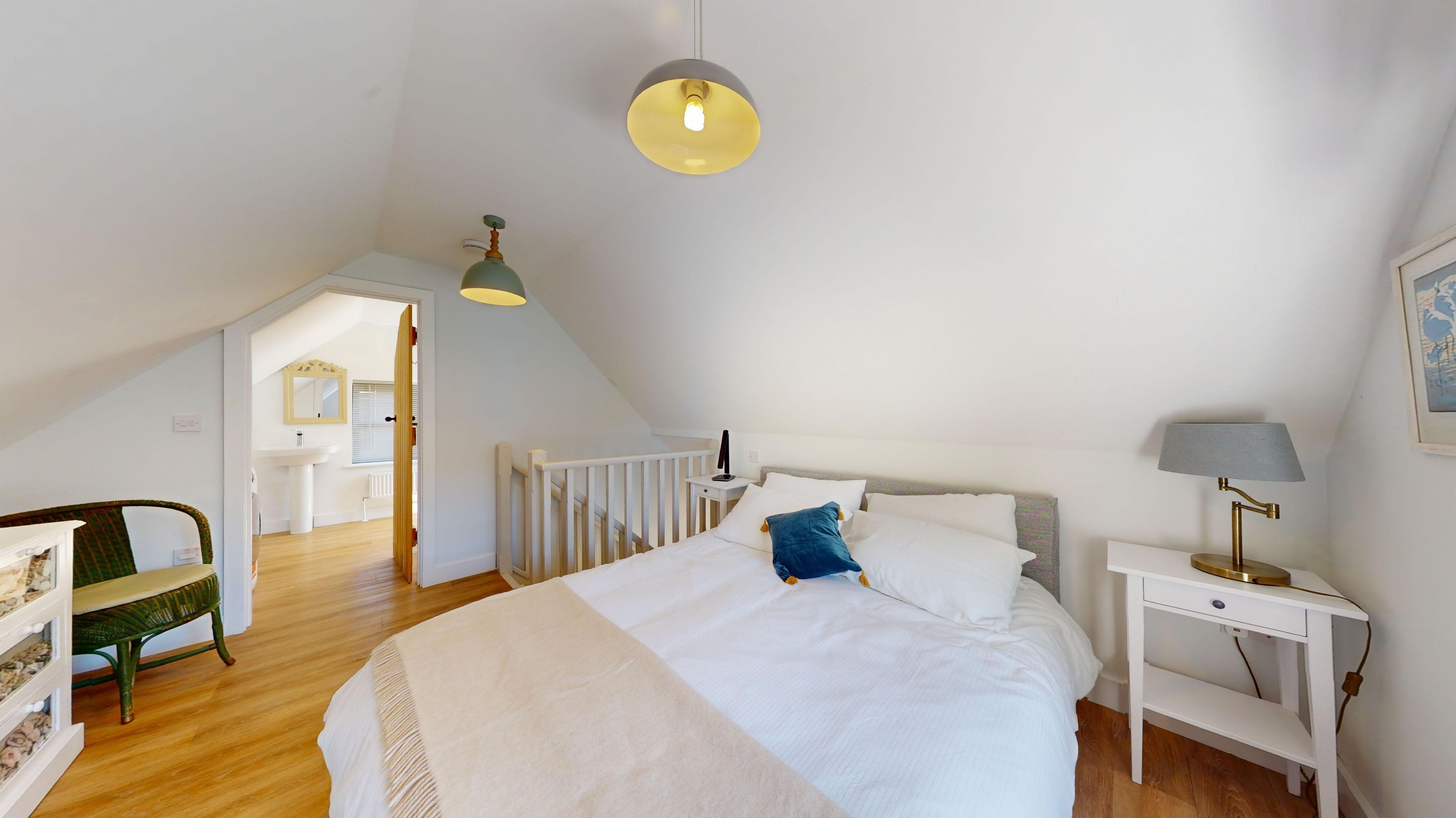 A bedroom with a bed, bedside table, lamp, and a view of the bathroom.