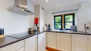 Een moderne keuken met witte kasten, een Bosch koelkast, een koffiezetapparaat en een raam met uitzicht op groen.