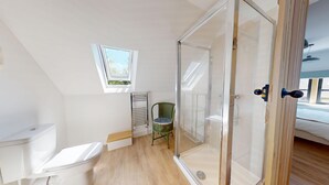 Een moderne badkamer met een douchecabine van glas, een toilet en een klein raam.