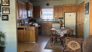 A spacious living room with a brown leather sofa, a wooden coffee table with a book, and a dining area with a table set for four. - Quaint, handicap accessible house in serene Lehigh, classified as a ghost town. (Lehigh)