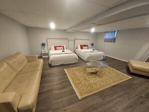 Two single beds with white bedding and red accent pillows, a beige leather sofa, and a round coffee table.