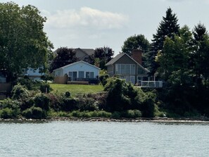 Enjoy serene lake views from this house's glass facade, surrounded by lush greenery and trees.