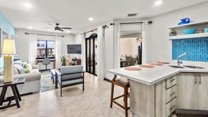 A modern kitchen with a central island, a dining area with a sofa and chairs, and a living room with a TV and a plant. - Jaco Beachfront Elegance at Tres Regalos Pristine Views in Lovely Jacó Beach (Jacó)