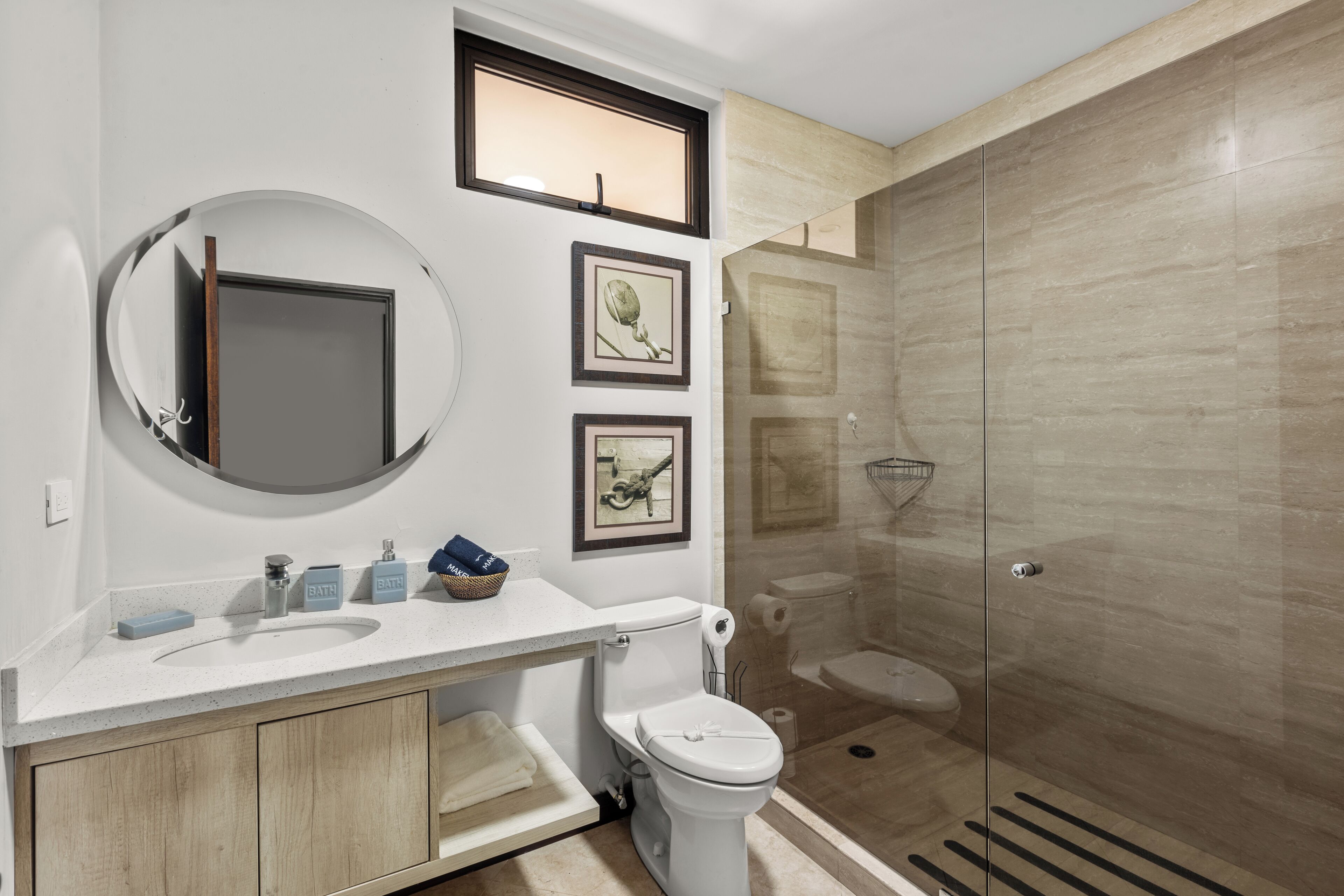A modern bathroom with a round mirror, a toilet, a shower, and a sink with a wooden cabinet.
