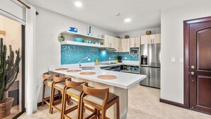 A modern kitchen with a central island, wooden bar stools, a refrigerator, and a cactus plant. - Jaco Beachfront Elegance at Tres Regalos Pristine Views in Lovely Jacó Beach (Jacó)